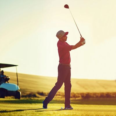 Golfer swinging club on a sunny course at sunset.