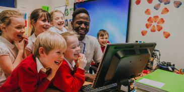Kids and teacher happily watching a computer screen.