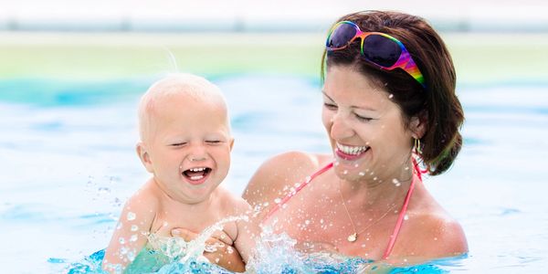 A joyful mother and baby playing in a swimming pool splashing water.