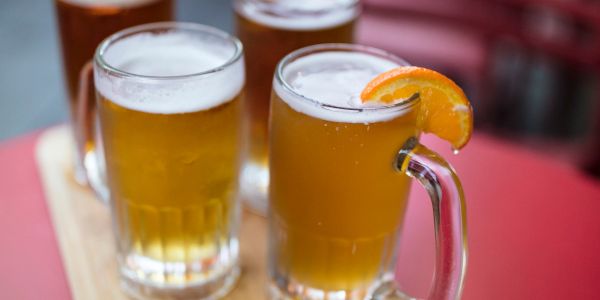 Four mugs of beer on a wooden tray, one garnished with an orange slice.