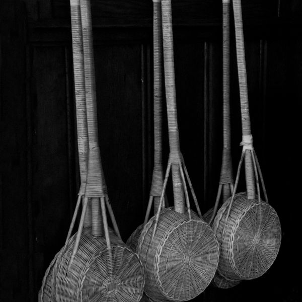 Four woven baskets hang by their handles on hooks against a dark wooden background.