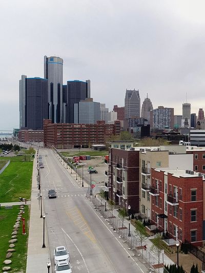 View of a city skyline with a tall glass building and residential apartments along a road.