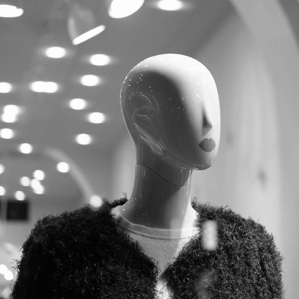 A faceless mannequin with lips painted on, dressed in a textured black jacket.