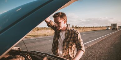 Man inspecting car engine on roadside with a concerned expression.