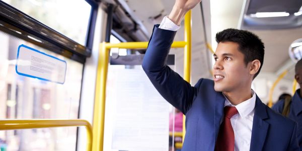 Young man in a suit holding a strap on a bus.