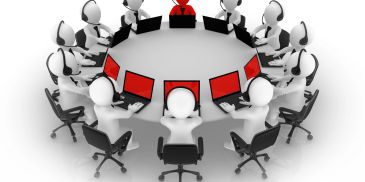 Roundtable meeting with laptops and a highlighted red figure.