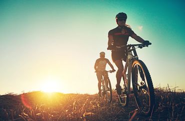 Two cyclists riding mountain bikes at sunset in an open field.