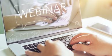 Laptop screen with the word WEBINAR on it and two hands on the keys