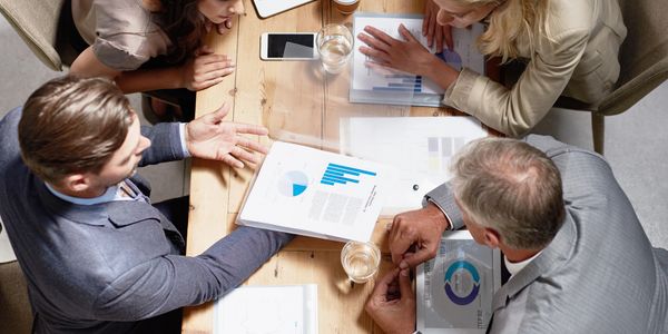 Four professionals discussing business charts around a wooden table.