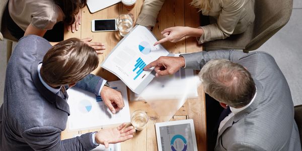 Four professionals collaborating over charts and data at a wooden table.