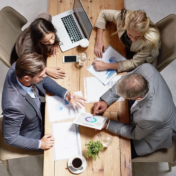 Four professionals discuss charts and graphs around a wooden table.