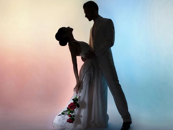 Silhouetted couple in elegant attire, the woman holding red roses, against a soft gradient backdrop.