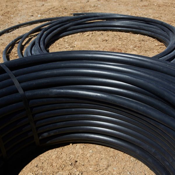 Coiled black plastic tubing on dirt ground.