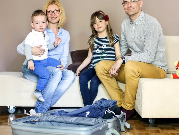 Family of four sitting on a couch with an open suitcase.