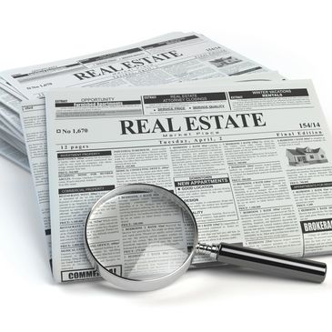 Magnifying glass over a real estate newspaper section focused on property listings.