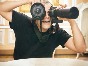 Man playfully using two cameras as binoculars, smiling.
