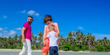 Family enjoying a sunny beach day with clear skies and palm trees.