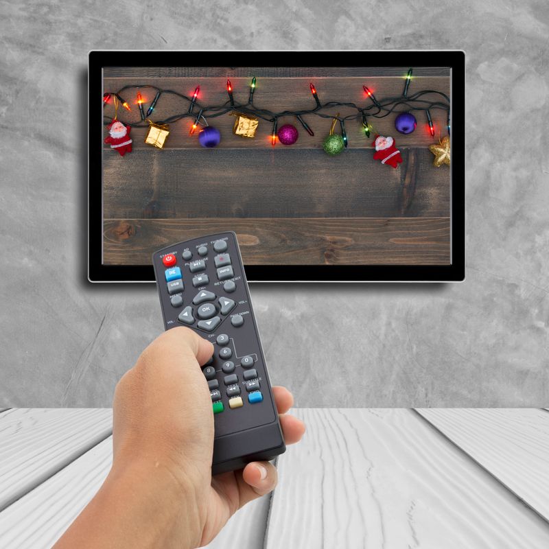 christmas decoration with hand holding remote control at television screen with concrete wall for background.