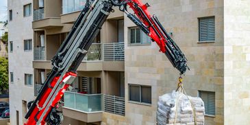 A red crane lifting a pallet of bags near an apartment building.