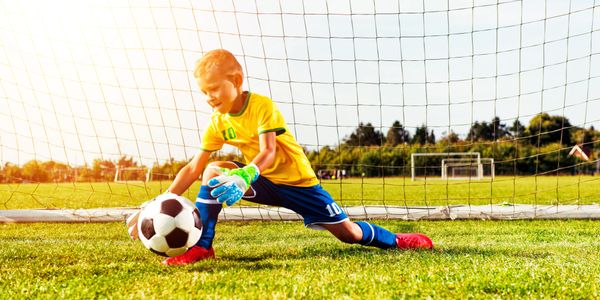 Young boy goalkeeper in yellow jersey saving a soccer ball near goalpost.