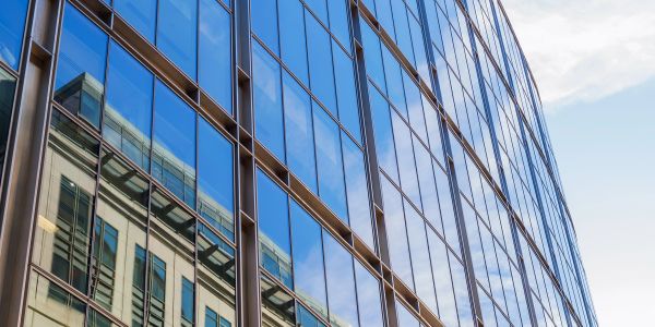 Reflection of a historic building on a modern glass skyscraper under a clear sky.