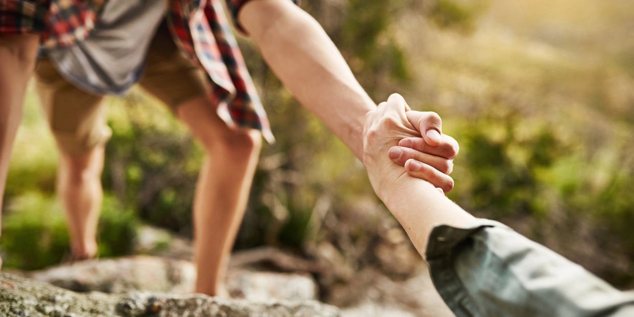 Two people holding hands during an outdoor hike, one helping the other climb.