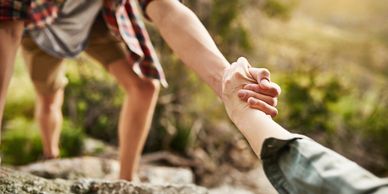 Person helping another climb a rocky hill by holding their hand.
