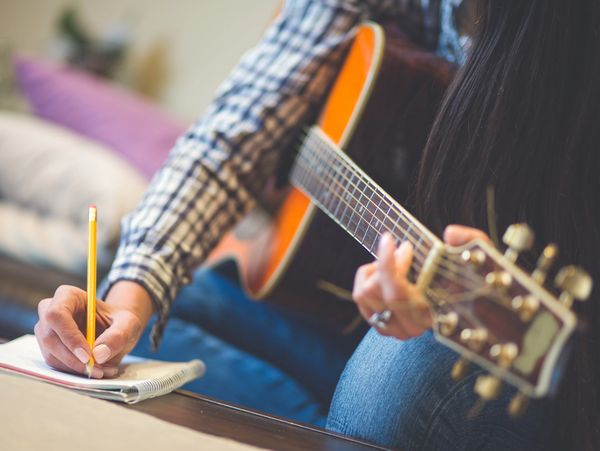 Person writing music while playing an acoustic guitar.