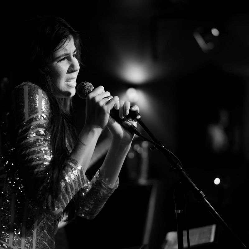 Young long haired caucasian woman, musician, singer and performer, singing on the stage. Black and white shoot
