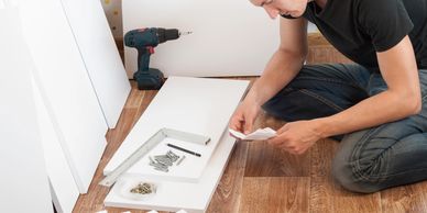 A man reading instructions while assembling white furniture on a wooden floor.