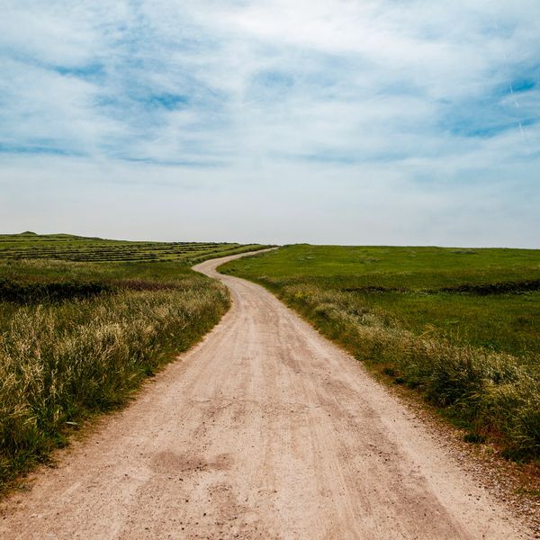 Dirt road winding through green fields under a blue sky.