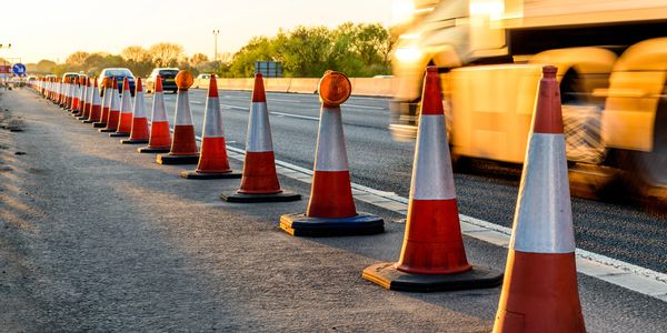 Traffic cones line a highway during sunset with vehicles passing by.
