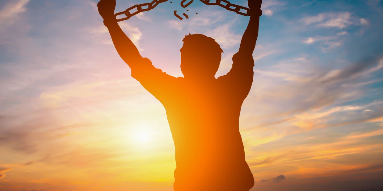 Silhouette of a person breaking free from chains at sunset.