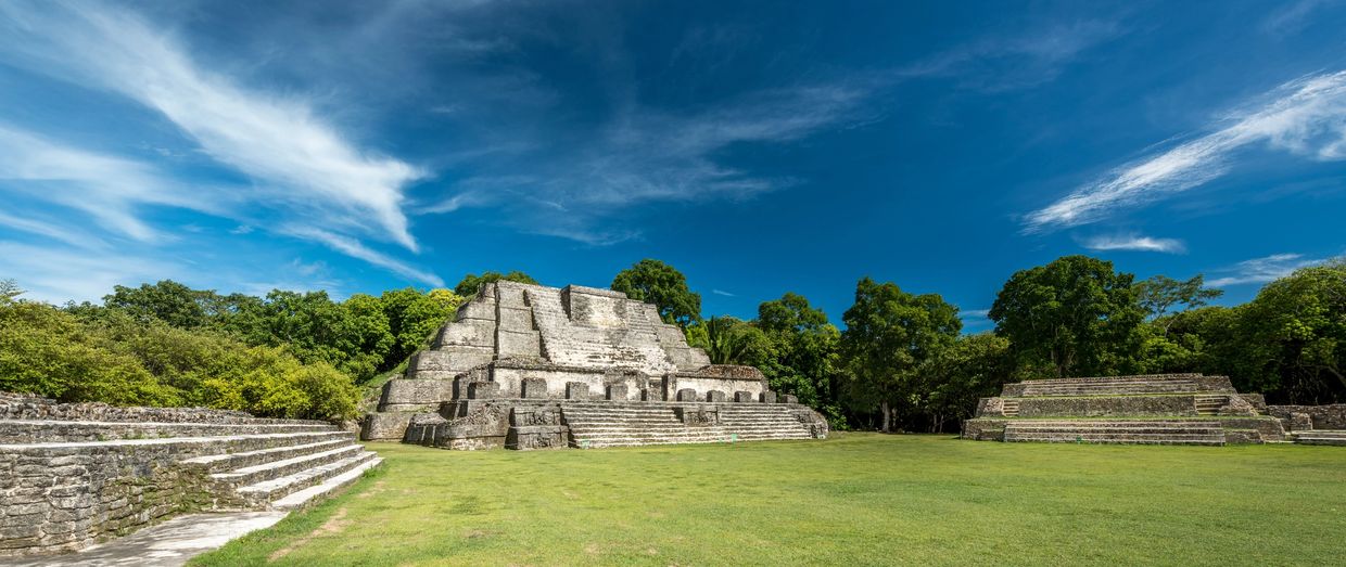 Ancient stone pyramids under a clear blue sky surrounded by greenery.