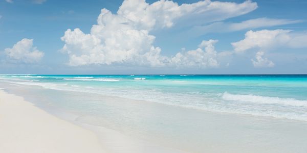 Playa con arena blanca y mar azul bajo un cielo nublado.