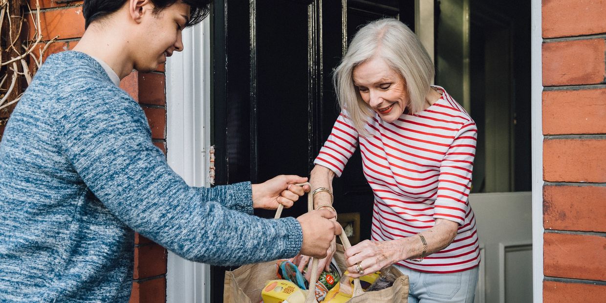 Young man delivering groceries to an elderly woman at her doorstep.