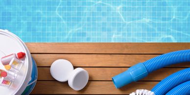 Pool cleaning supplies and chemicals on a wooden deck beside a clear swimming pool.