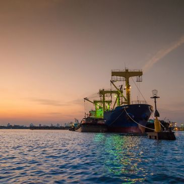 Cargo ships docked at harbor during sunset with calm waters.