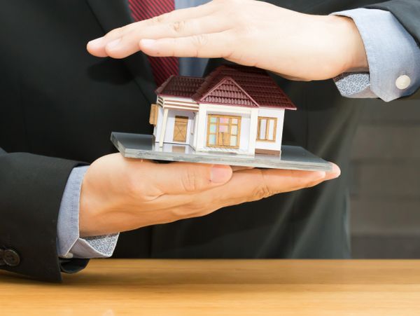 Person in suit protecting a miniature house model with hands.