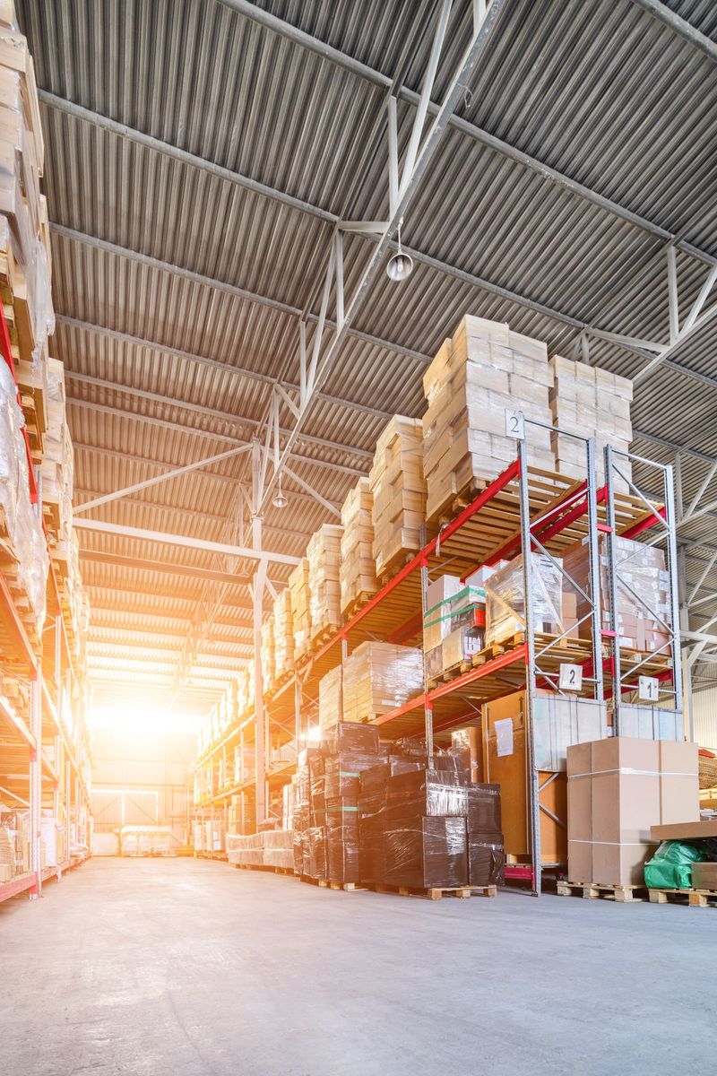 Large industrial warehouse. Long shelves with a variety of boxes and containers. Bright sunlight.