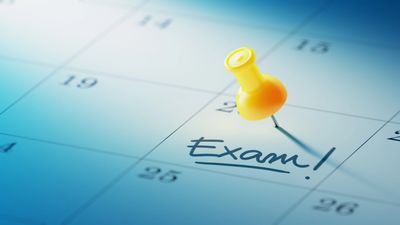 Yellow pushpin marks an exam date on a calendar.