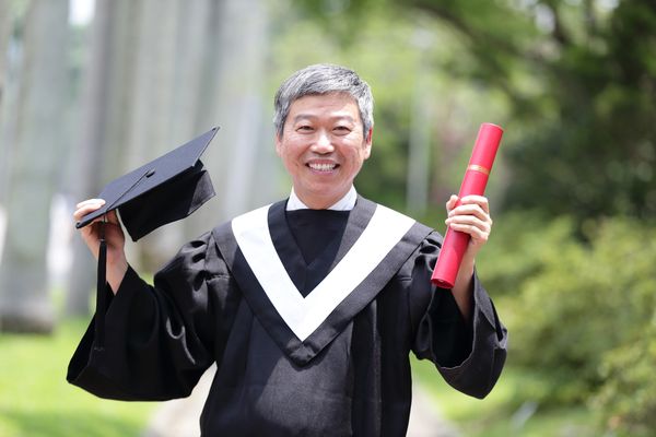 Smiling graduate in cap and gown holding diploma.