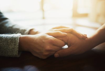 Two people holding hands in a comforting manner.