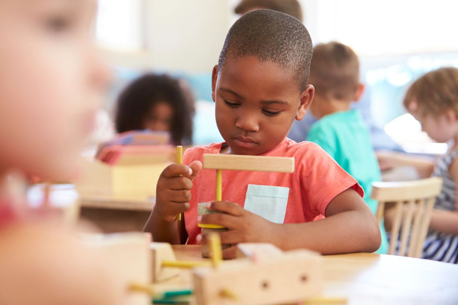 A focused boy plays with wooden building blocks in a classroom.