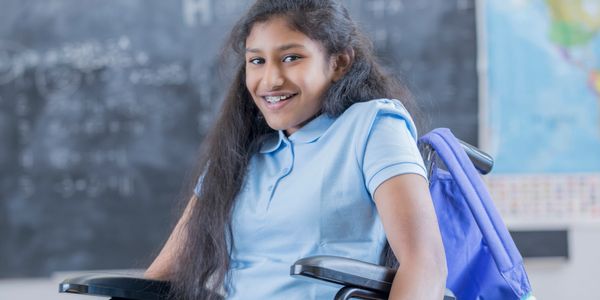 Smiling girl in a wheelchair in a classroom setting.