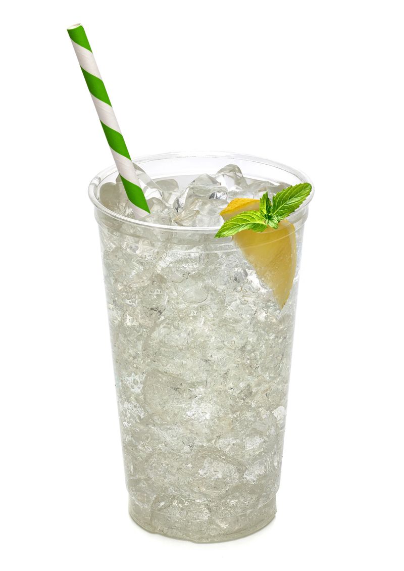 Soda with ice, slice of lemon wedge and mint in takeaway cup on white background