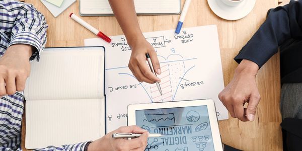 Three people collaborating on digital marketing using a tablet and notes.