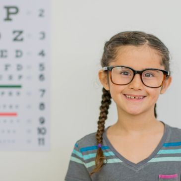Smiling girl wearing glasses with an eye chart in the background.