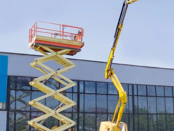 Two extended aerial work platforms parked outside a building on a sunny day.