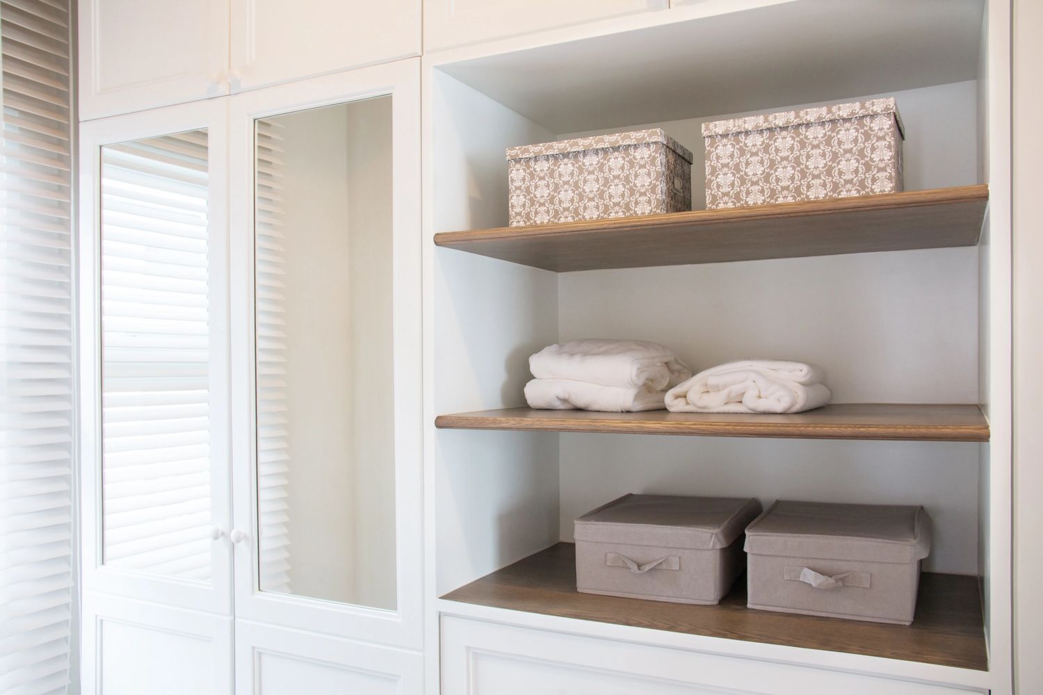 Neatly organized white closet shelves with boxes and folded towels.